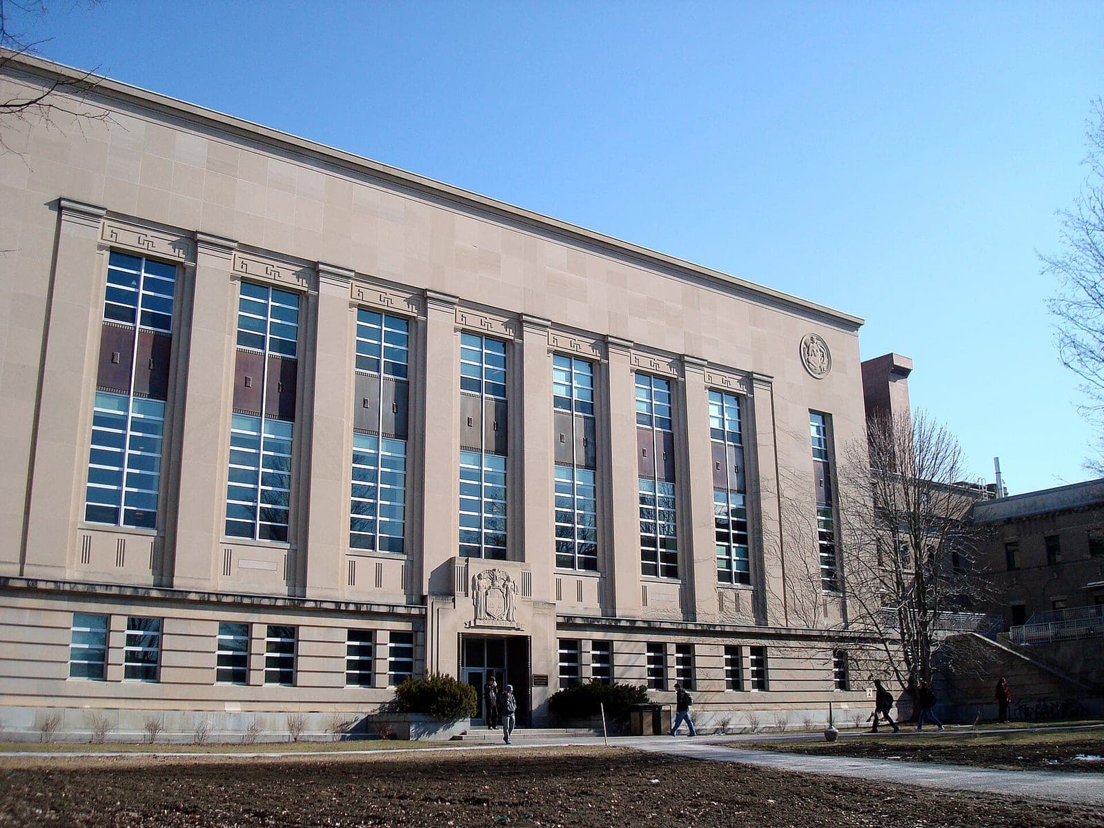 The stone facade of Mann Library at Cornell University under a blue sky, with students walking past