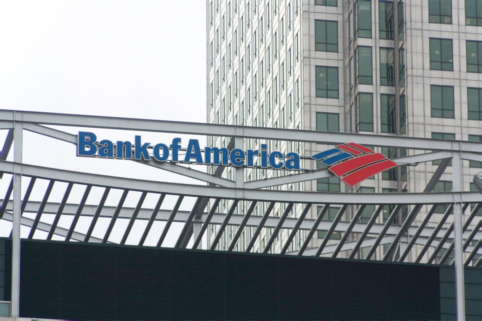 A blue Bank of America sign with the red and blue flag logo on a steel frame in front of an office tower at Canary Wharf, London