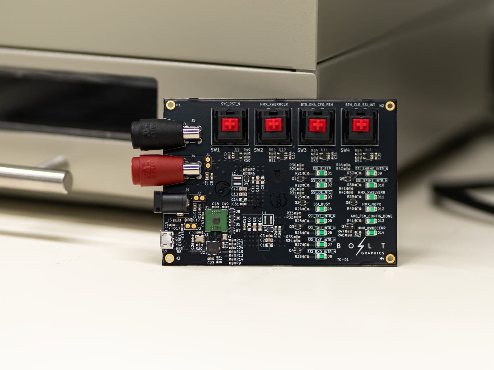 A black circuit board with four red keyboard-style switches, rows of small green lights, and a small green chip, with the Bolt Graphics logo printed in the corner