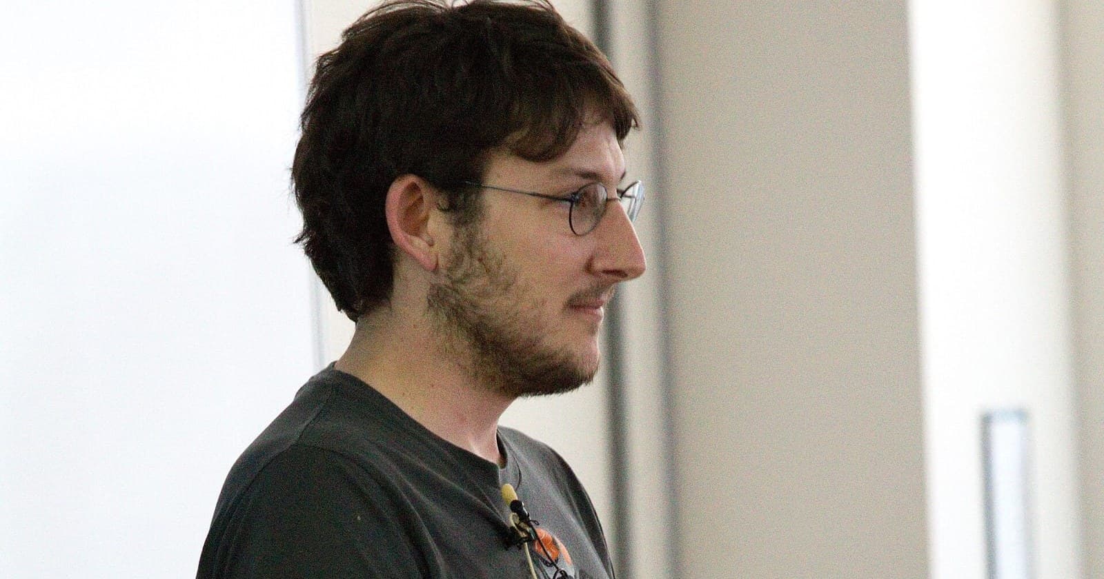 Ryan Dahl, creator of Node.js and Deno, in profile wearing glasses and a dark T-shirt with a clip-on microphone while giving a talk.