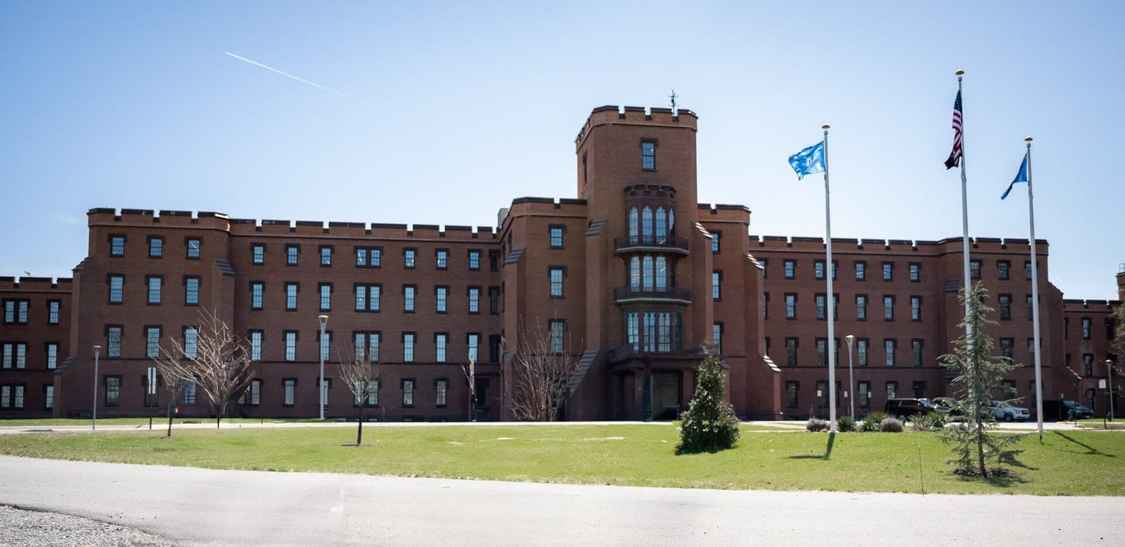 A long red-brick building with a central tower and flagpoles flying the US flag on the St. Elizabeths campus, home of DHS headquarters in Washington