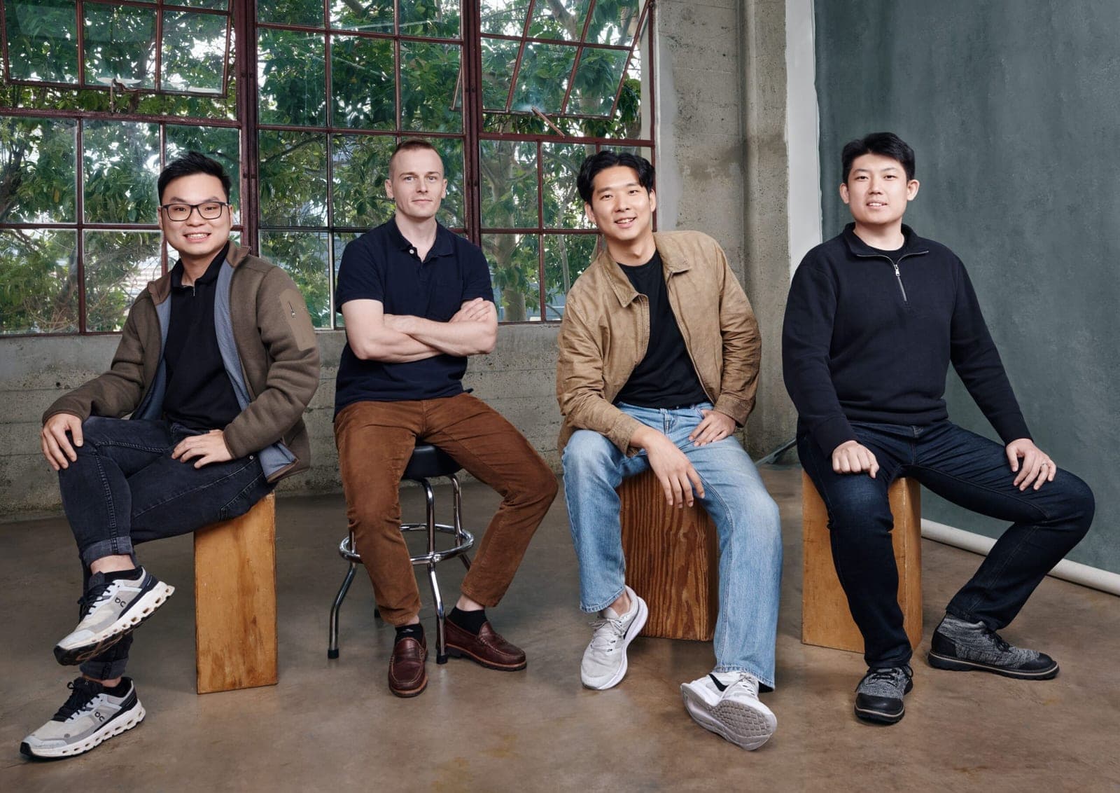 Four members of the Dream Labs team sit on stools and wooden blocks in a bright studio with large industrial windows behind them
