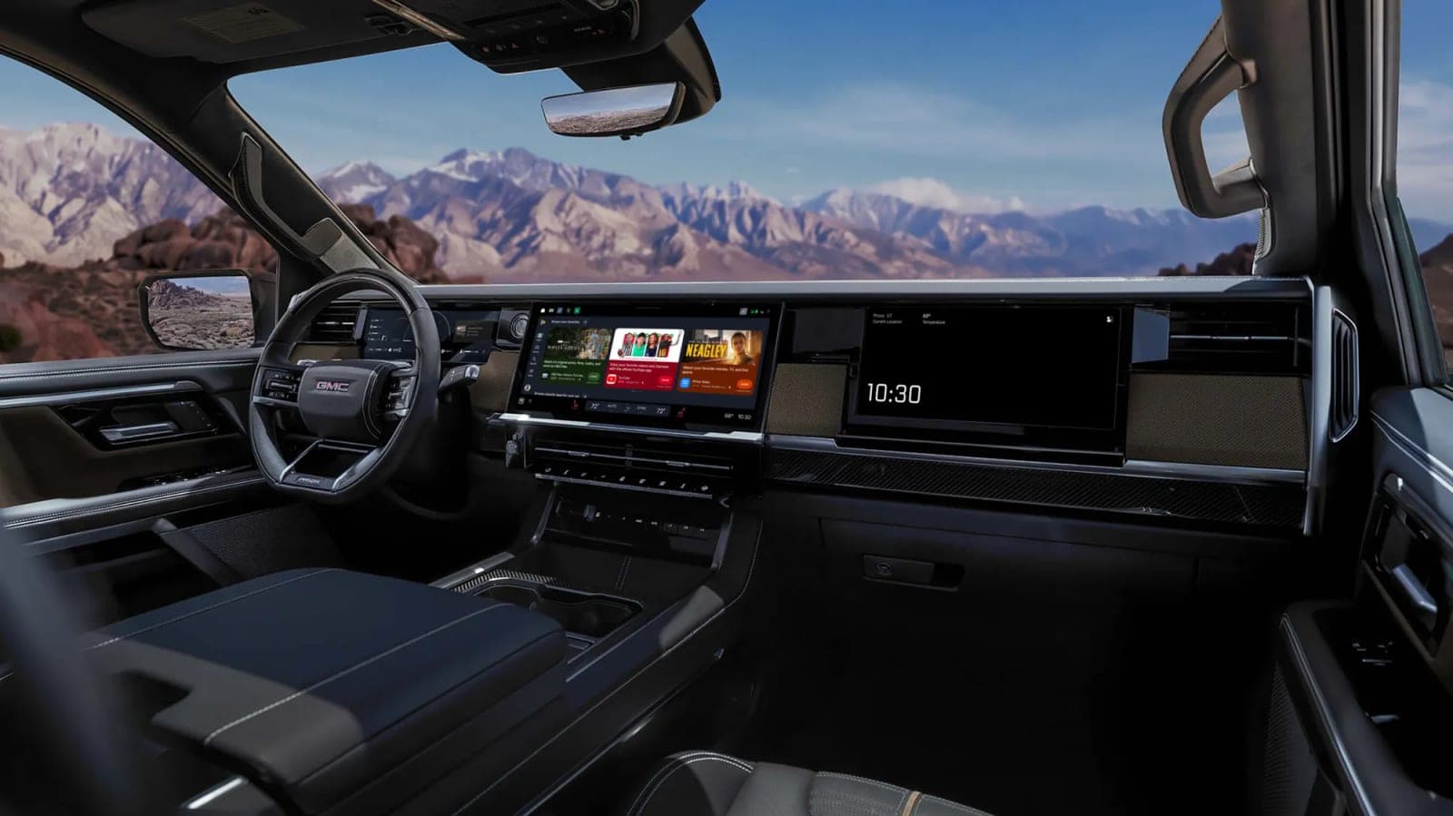 The cabin of a GMC pickup with a wide center touchscreen showing the Google Play Store, and desert mountains visible through the windshield