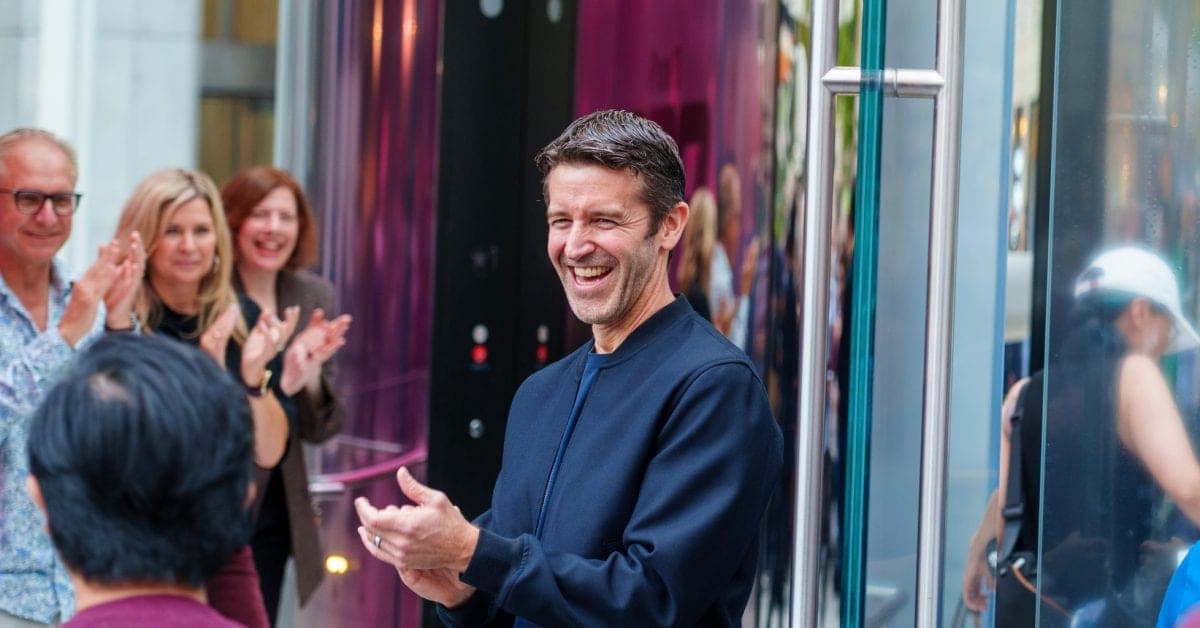 John Ternus smiling and clapping while standing outside an Apple retail location, surrounded by applauding colleagues.