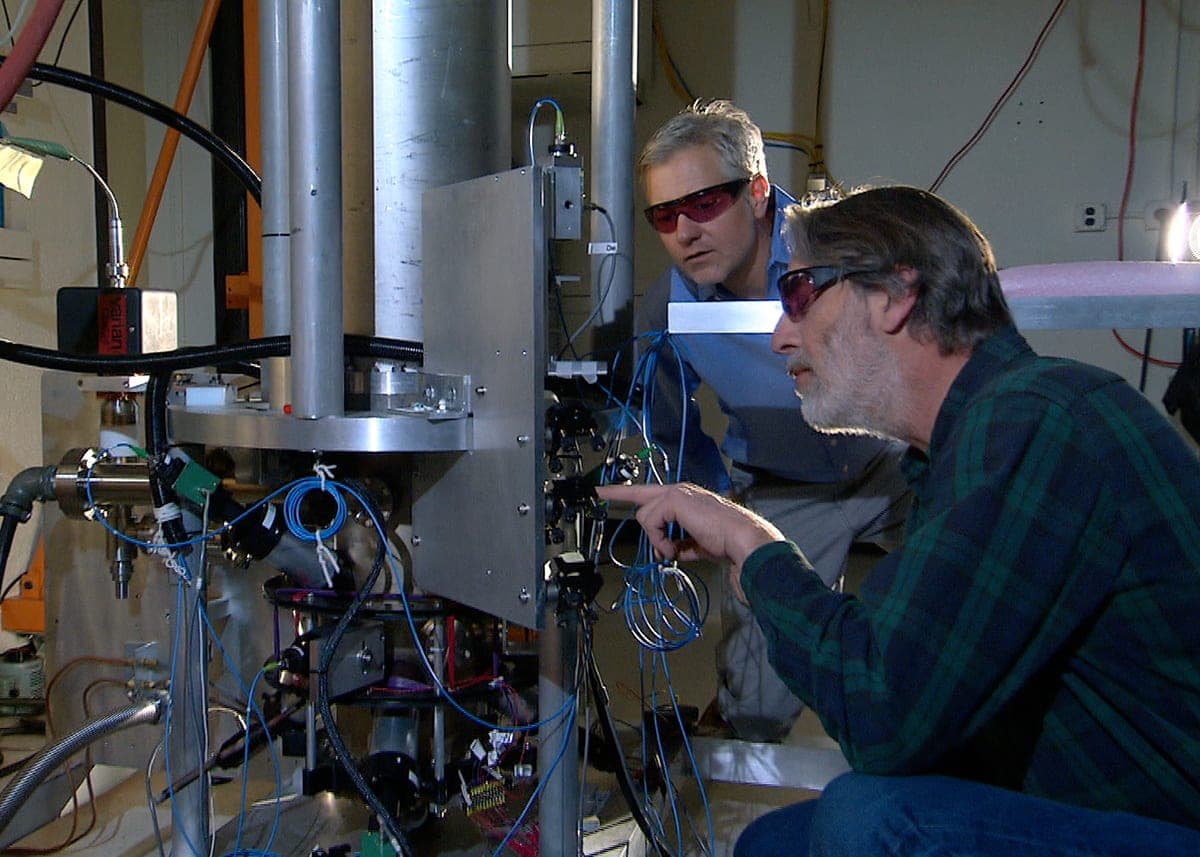 Two NIST physicists in tinted safety glasses inspect the wiring of the NIST-F2 cesium fountain atomic clock in a laboratory
