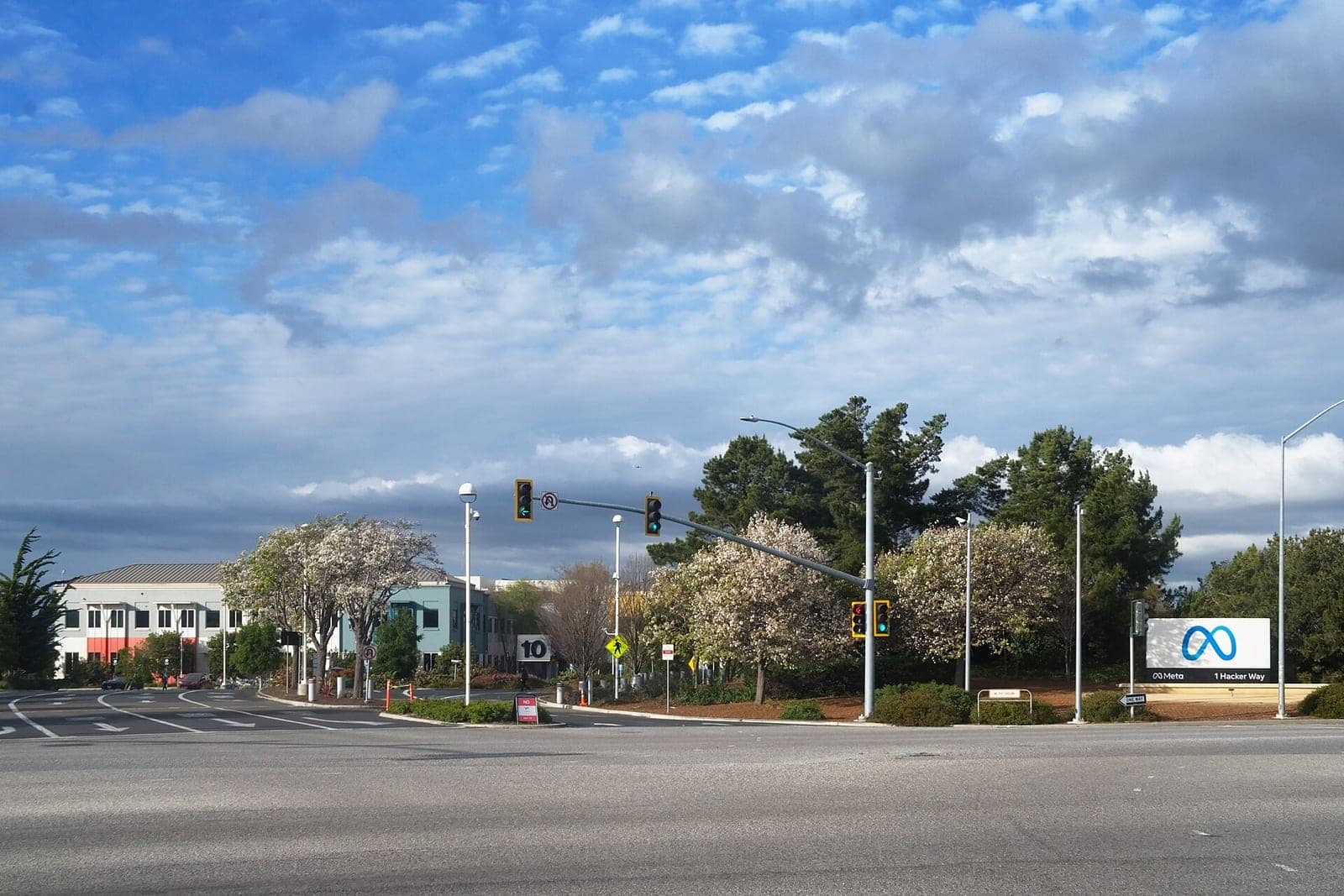 The Meta sign reading 1 Hacker Way at the entrance to the company's Menlo Park campus, with office buildings and trees behind it
