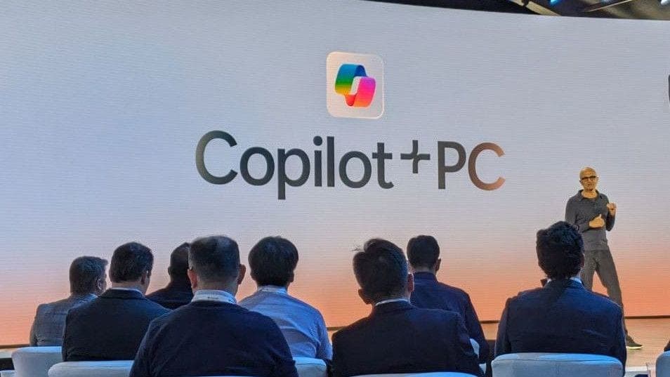 A presenter on stage in front of a large Copilot+PC branding screen at a Microsoft event