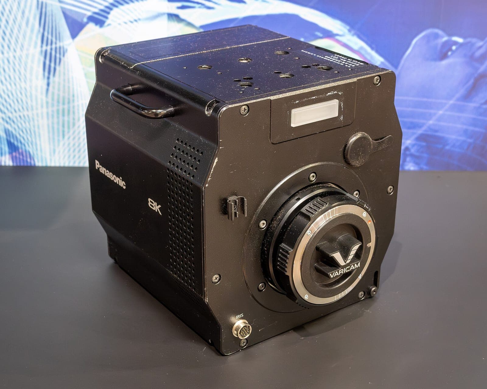 A professional black cinema camera with an 8K lens mount sitting on a table in a studio