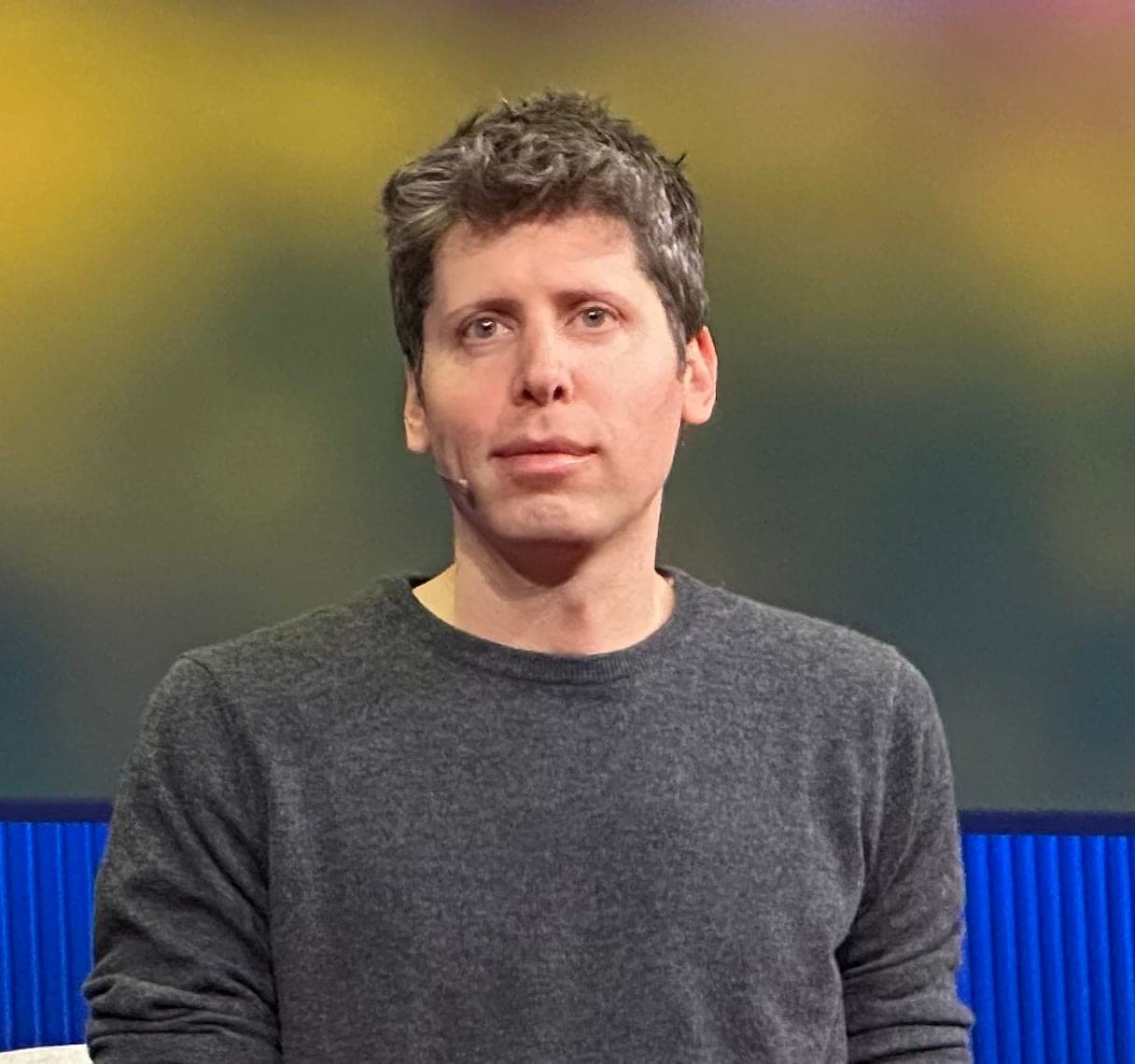 Sam Altman speaking on stage with a microphone headset