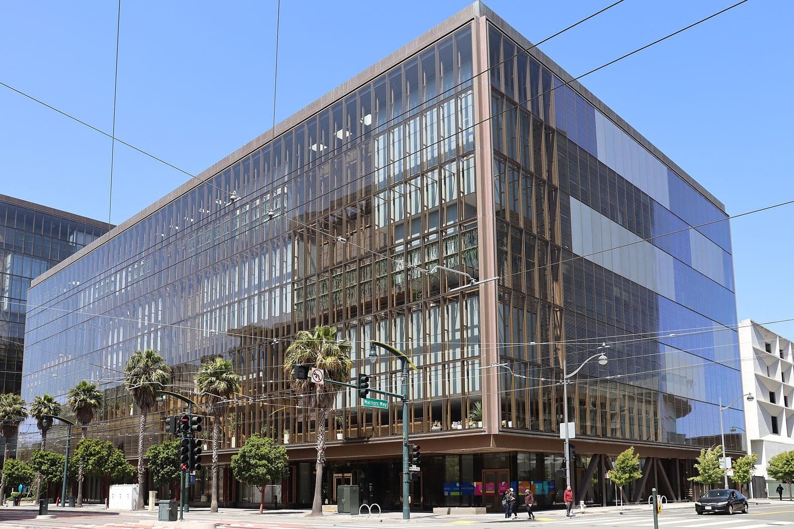 A seven-story glass office building at 1515 Third Street in San Francisco's Mission Bay, which housed OpenAI's headquarters in 2025, with palm trees and traffic lights at the corner