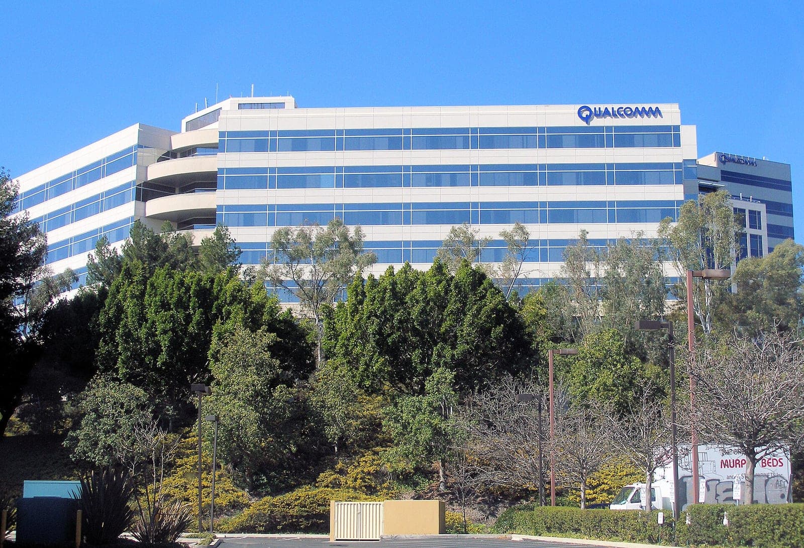 Qualcomm's headquarters building in San Diego, with the Qualcomm logo near the roof, behind trees