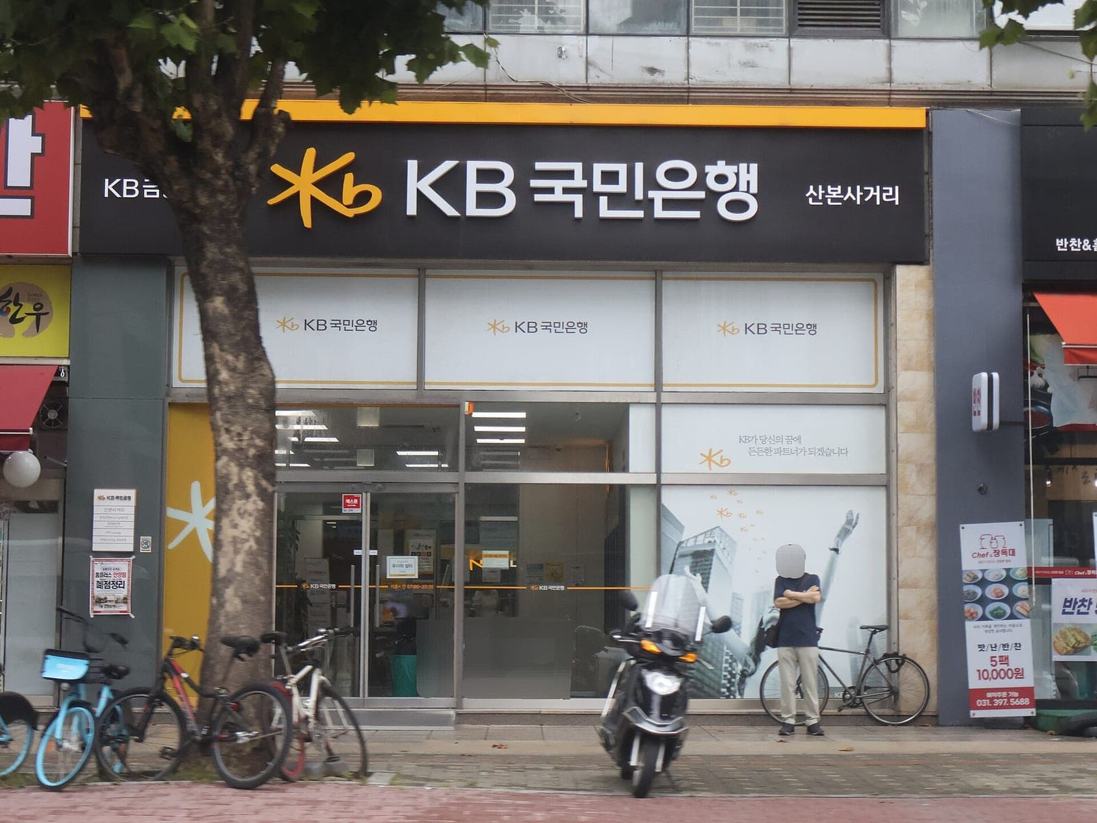 Street view of a KB Kookmin Bank branch in Gunpo, South Korea, with its yellow and black sign above the entrance
