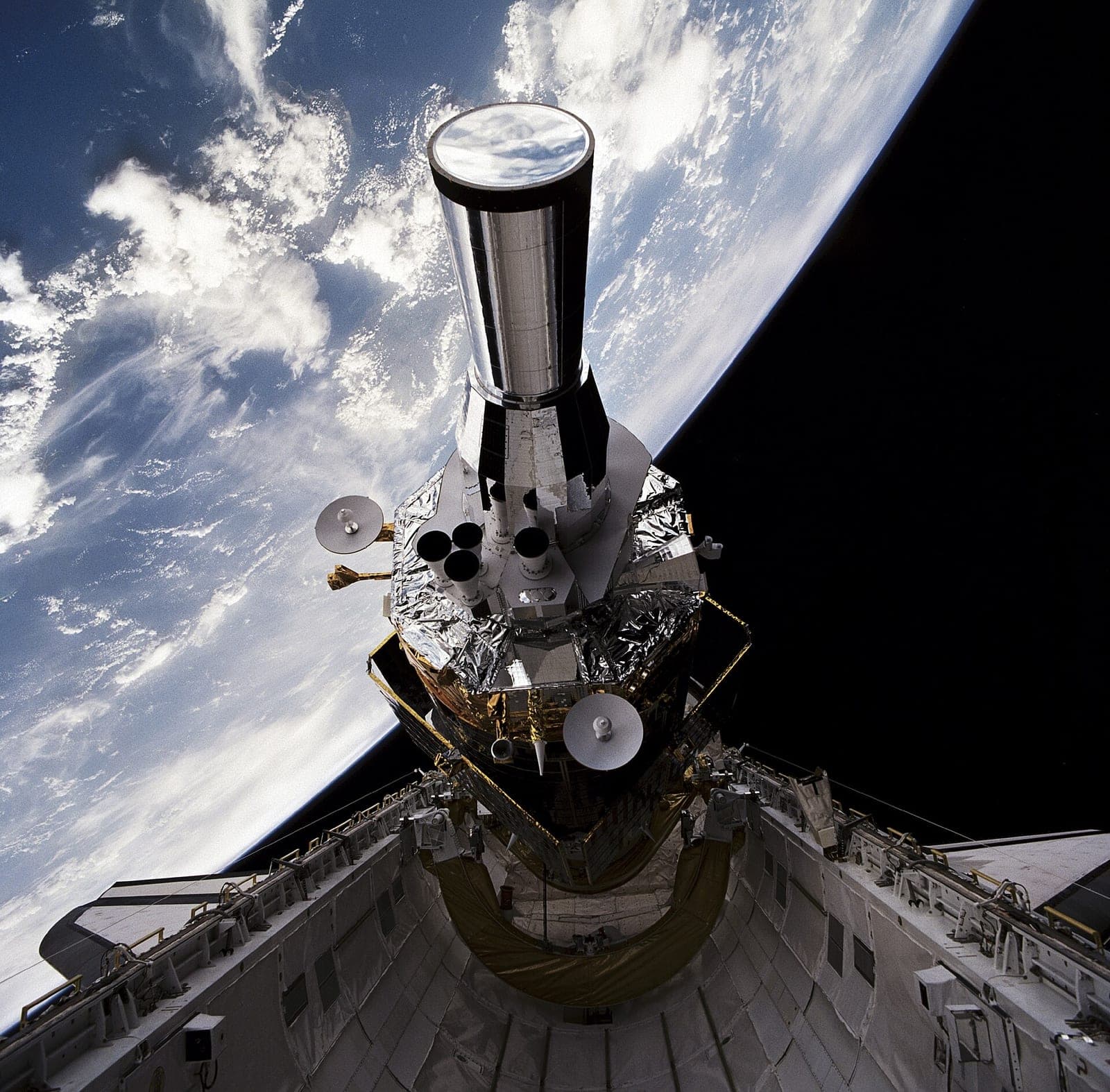 A Defense Support Program satellite with its upper stage rising out of Space Shuttle Atlantis's payload bay, with Earth's clouds and the horizon behind it, during mission STS-44 in 1991