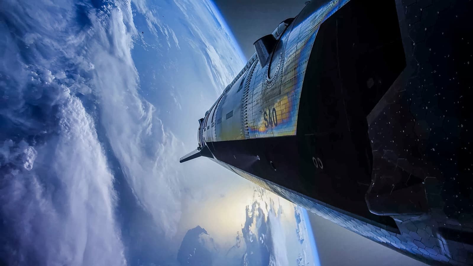 SpaceX's Starship spacecraft, marked S40, seen from a low angle against the curvature of Earth and clouds below, with stars visible in the dark sky above.
