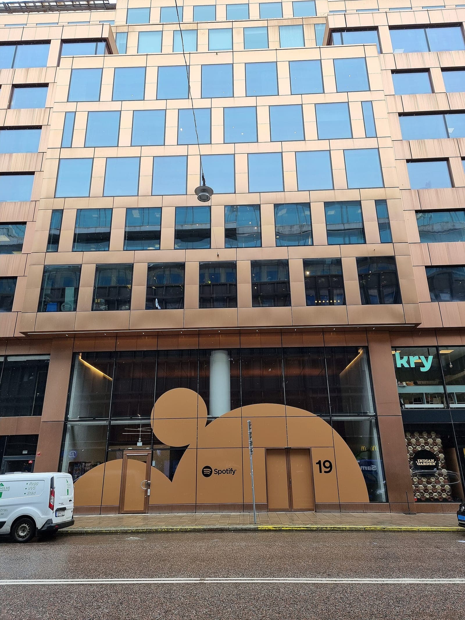 The glass and copper-colored front of a Stockholm office building with a large brown graphic and the Spotify logo at street level