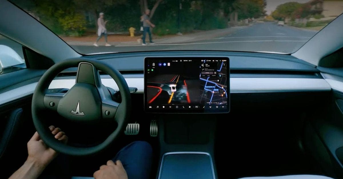 View from the driver's seat of a Tesla, with a hand on the steering wheel and the center screen showing the car's view of the road and a map