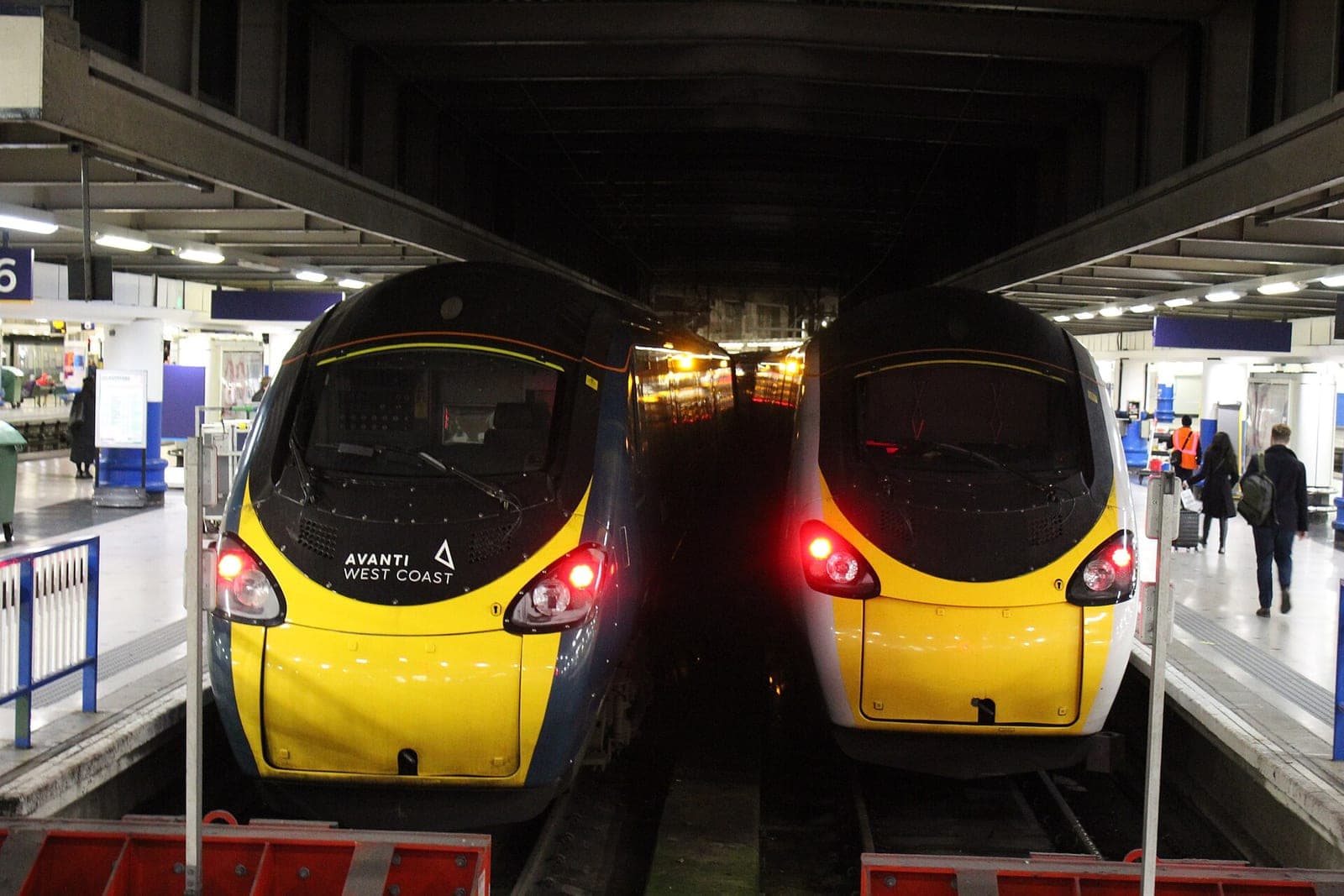 Two yellow-nosed Avanti West Coast Pendolino trains side by side at the platforms of London Euston station, with passengers walking on the right
