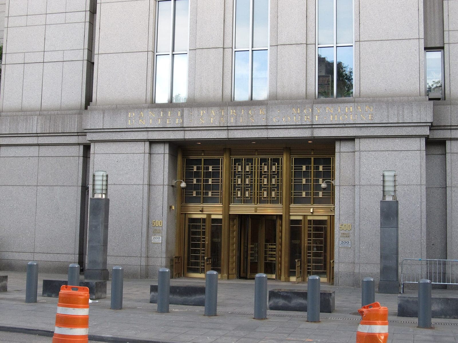 The granite entrance of the Daniel Patrick Moynihan United States Courthouse at 500 Pearl Street in Manhattan, with bronze doors and orange traffic barrels on the sidewalk.