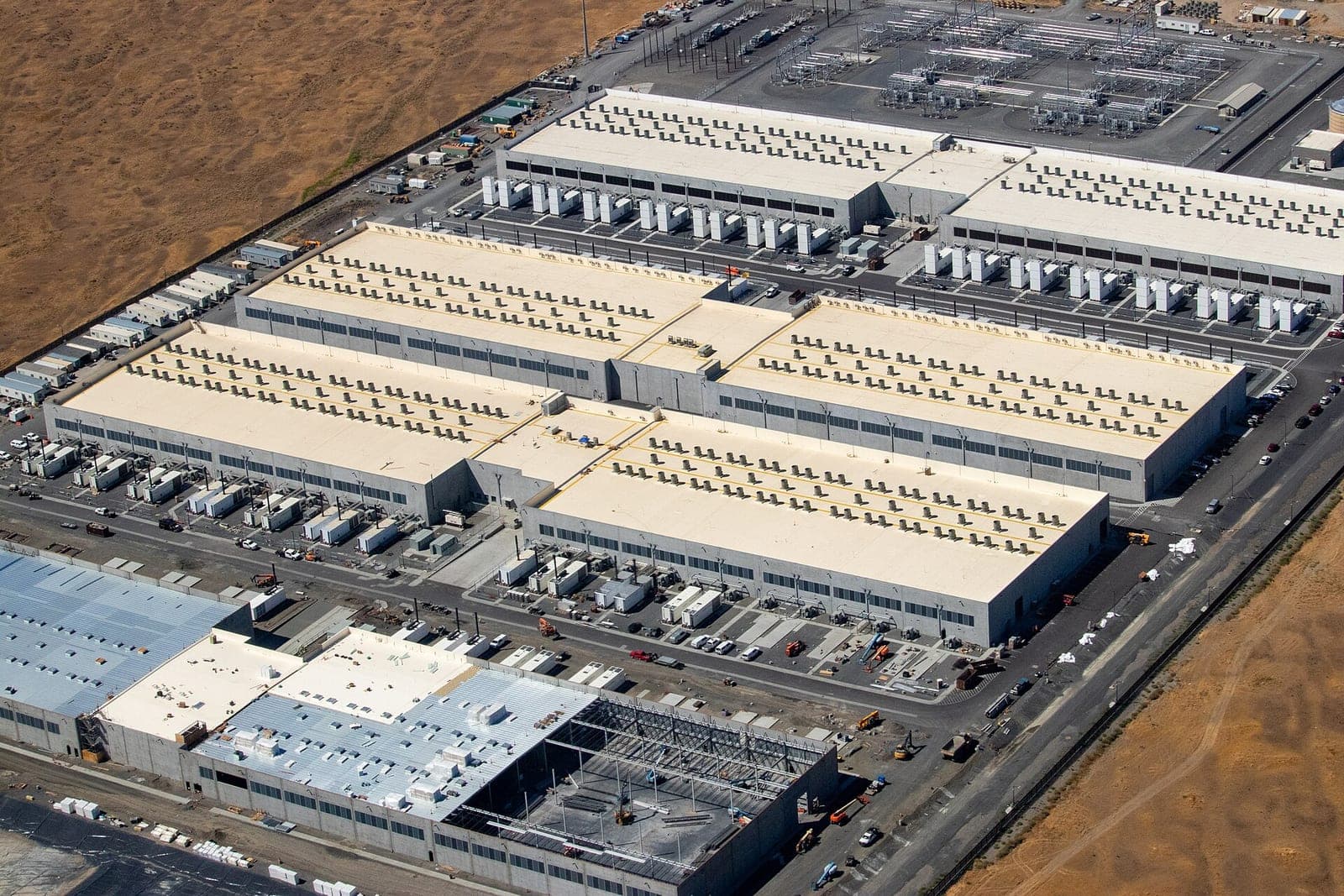 Aerial view of large Amazon Web Services data center buildings in Morrow County, Oregon, with rows of rooftop equipment, generators and a substation