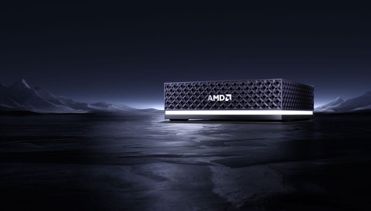 A dark, compact AMD-branded mini-PC device with a perforated grille pattern and illuminated base, shown on a reflective dark surface
