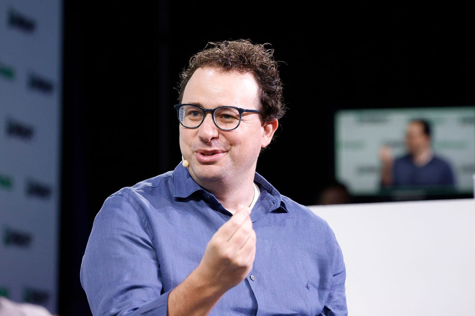 Anthropic CEO Dario Amodei, wearing glasses and a blue shirt, speaking on stage at TechCrunch Disrupt 2023