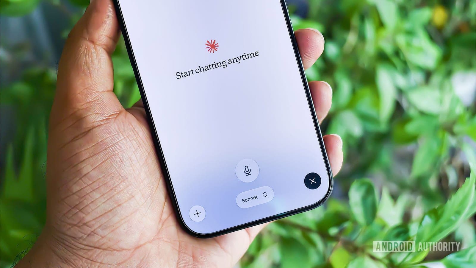 A hand holding a smartphone displaying the Claude app's voice chat interface, with the Sonnet model selector visible at the bottom of the screen.