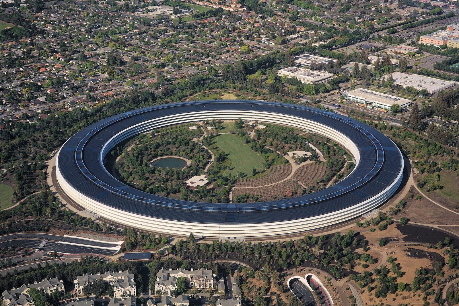 Aerial view of Apple Park, Apple's ring-shaped headquarters in Cupertino, surrounded by trees and houses.