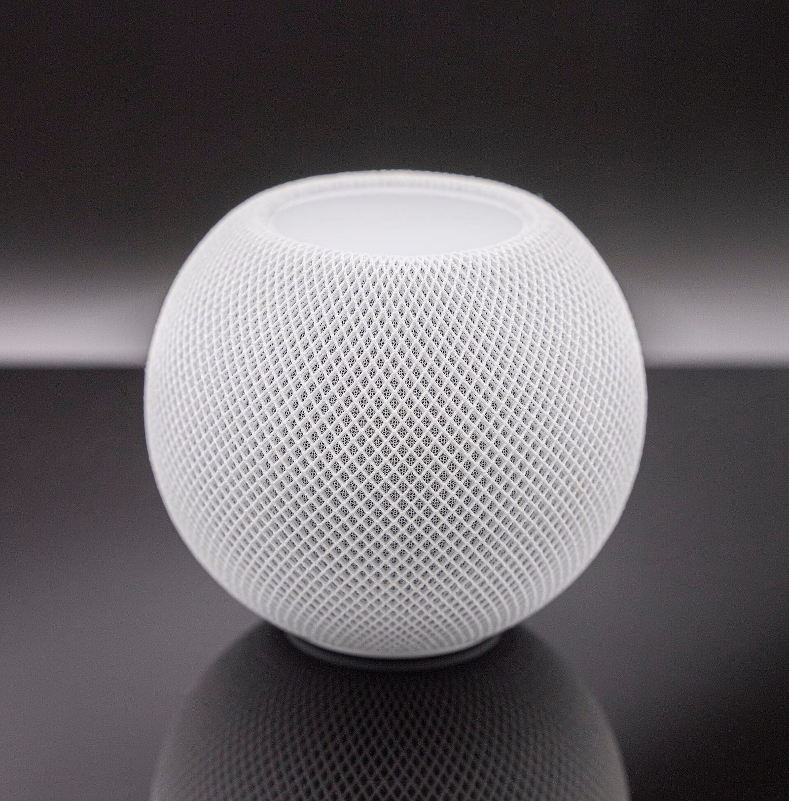 A white Apple HomePod mini smart speaker on a dark reflective surface