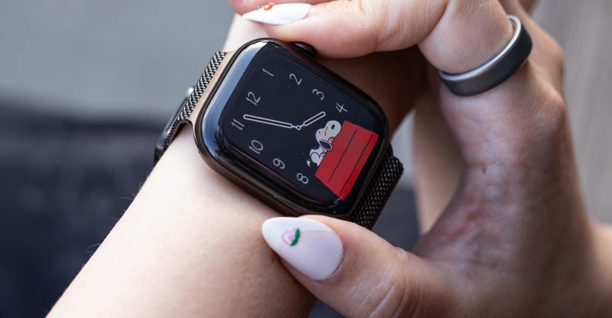 A person's wrist wearing a black Apple Watch with a Snoopy watch face, held up by their other hand.
