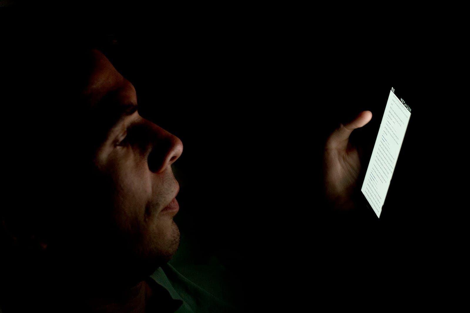 A person's face lit up by the glow of a smartphone screen in a dark room