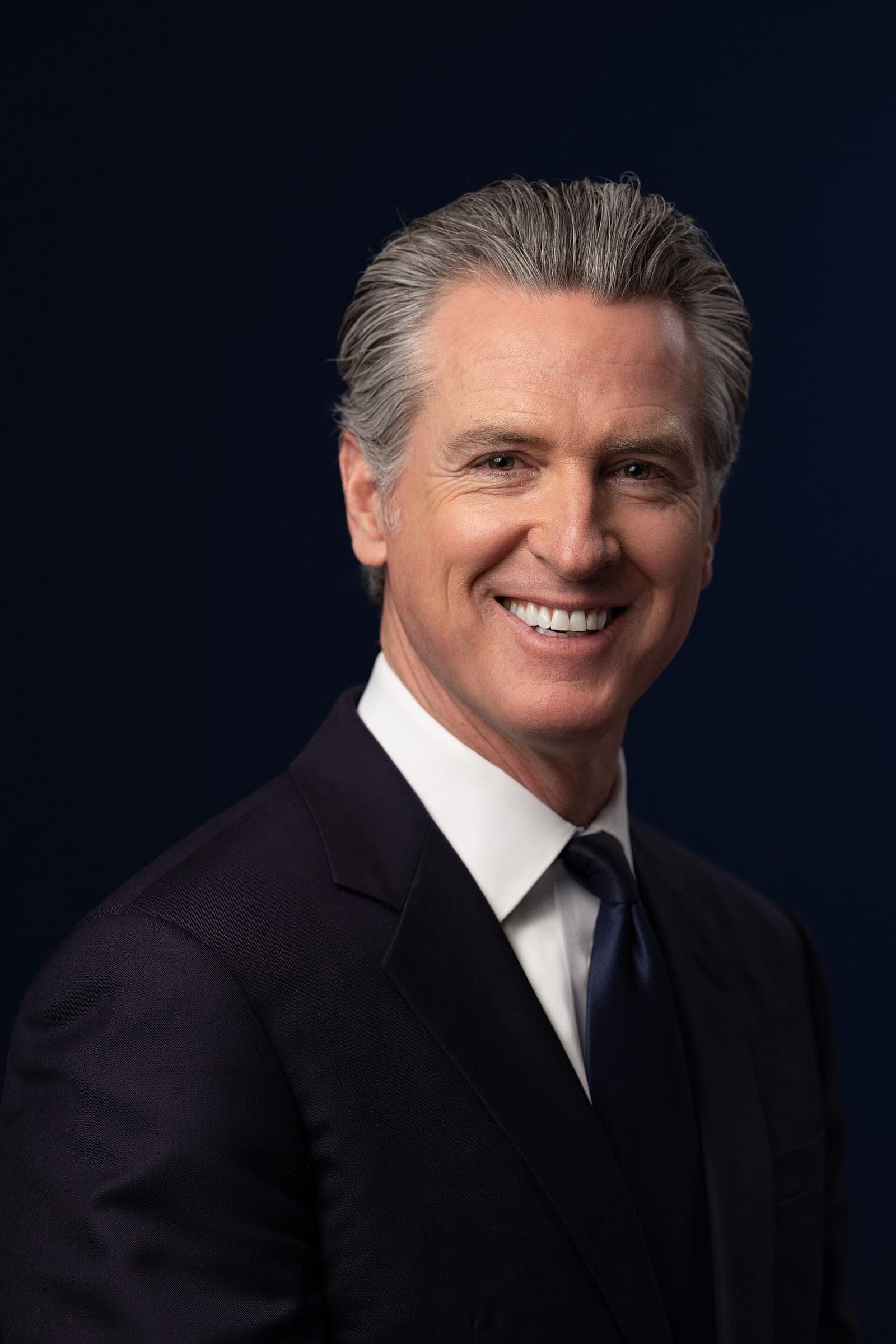 Official portrait of California Governor Gavin Newsom in a dark suit against a navy background
