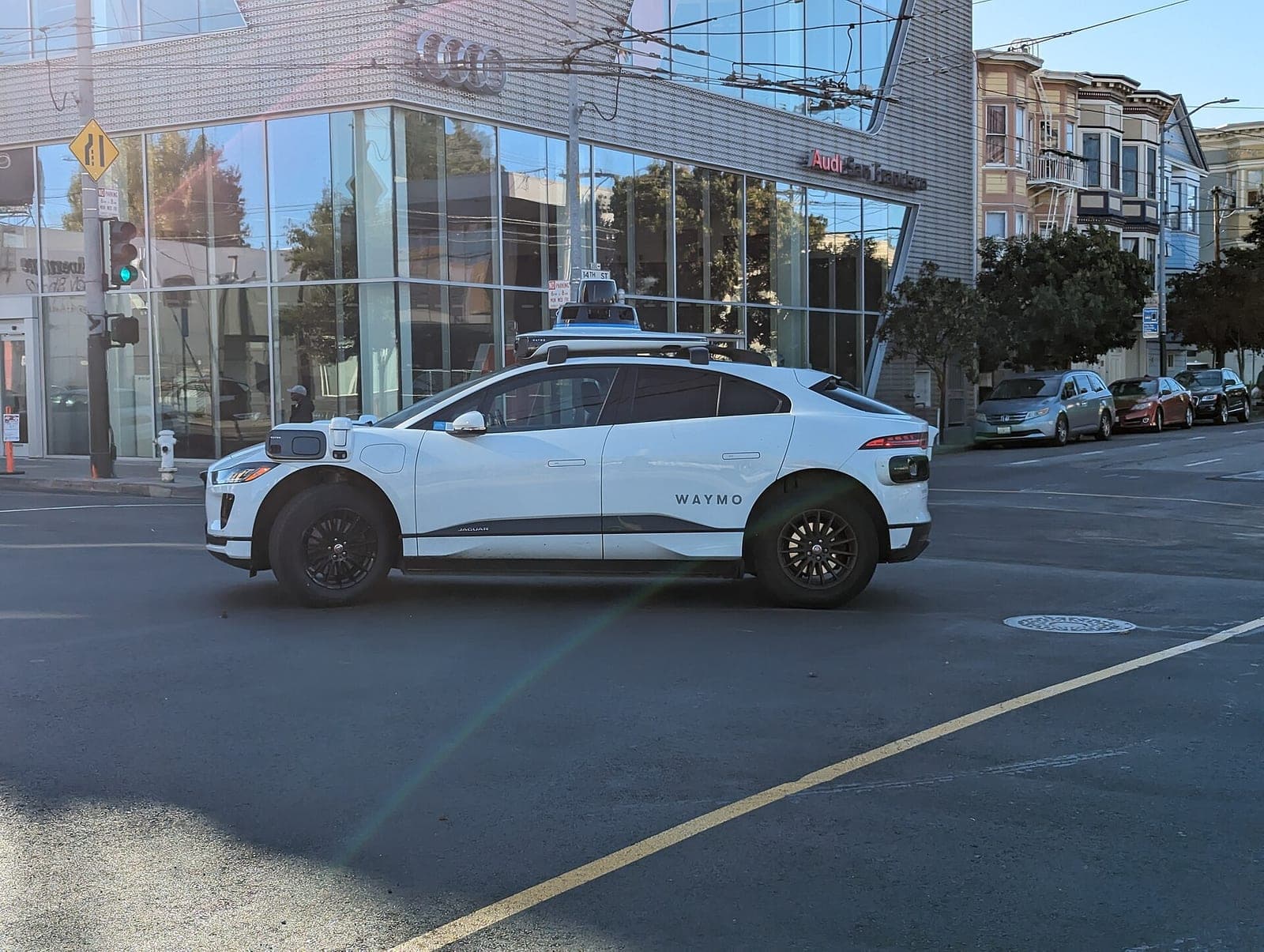A white Waymo Jaguar I-Pace robotaxi with roof sensors crossing an intersection in San Francisco