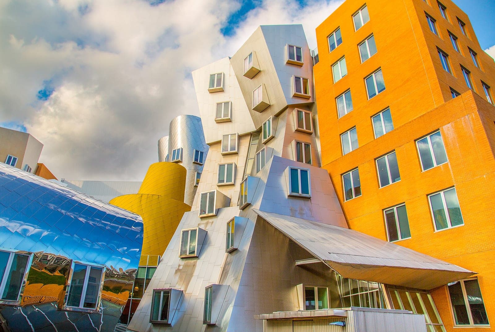 The Ray and Maria Stata Center at MIT, home of the Computer Science and Artificial Intelligence Laboratory, with tilted silver walls and an orange brick tower under a cloudy sky