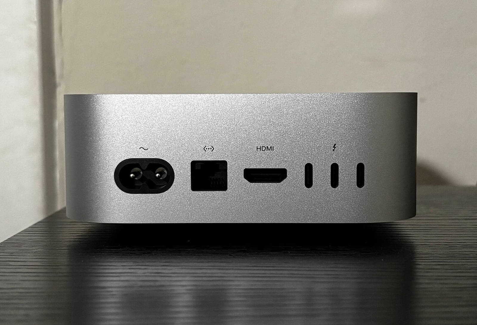 The back of a silver Mac mini on a dark wooden table, showing its power socket, Ethernet port, HDMI port and three USB-C ports.