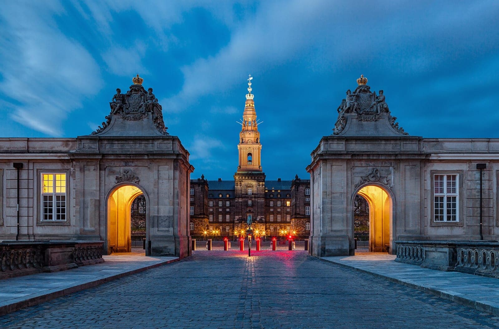 Christiansborg Palace in Copenhagen, home of the Danish parliament, lit up at dusk and seen through the arched gate pavilions of the Marble Bridge