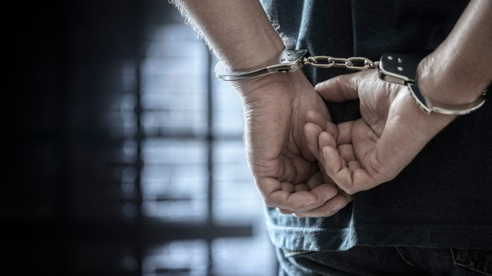 Close-up of a person's handcuffed wrists behind their back.
