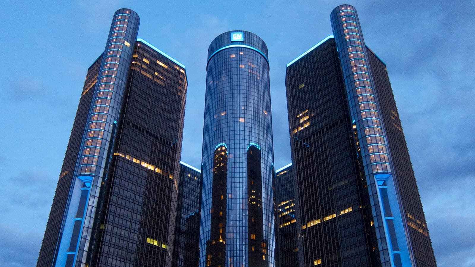 The glass towers of General Motors' Renaissance Center headquarters in Detroit at dusk, with the GM logo on the central tower