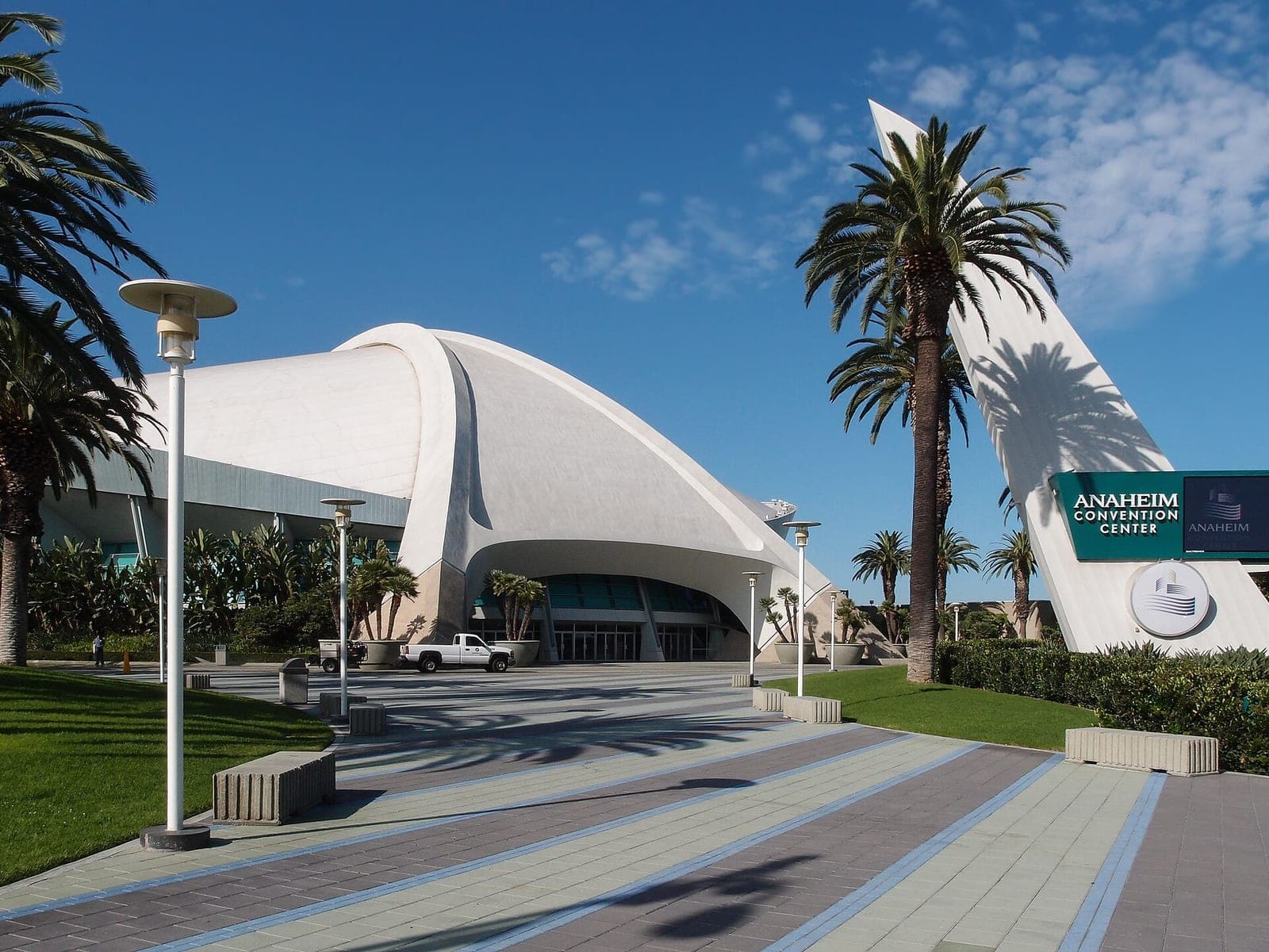 The white curved roof of the Anaheim Convention Center under a blue sky, with palm trees and a green Anaheim Convention Center sign on the right.