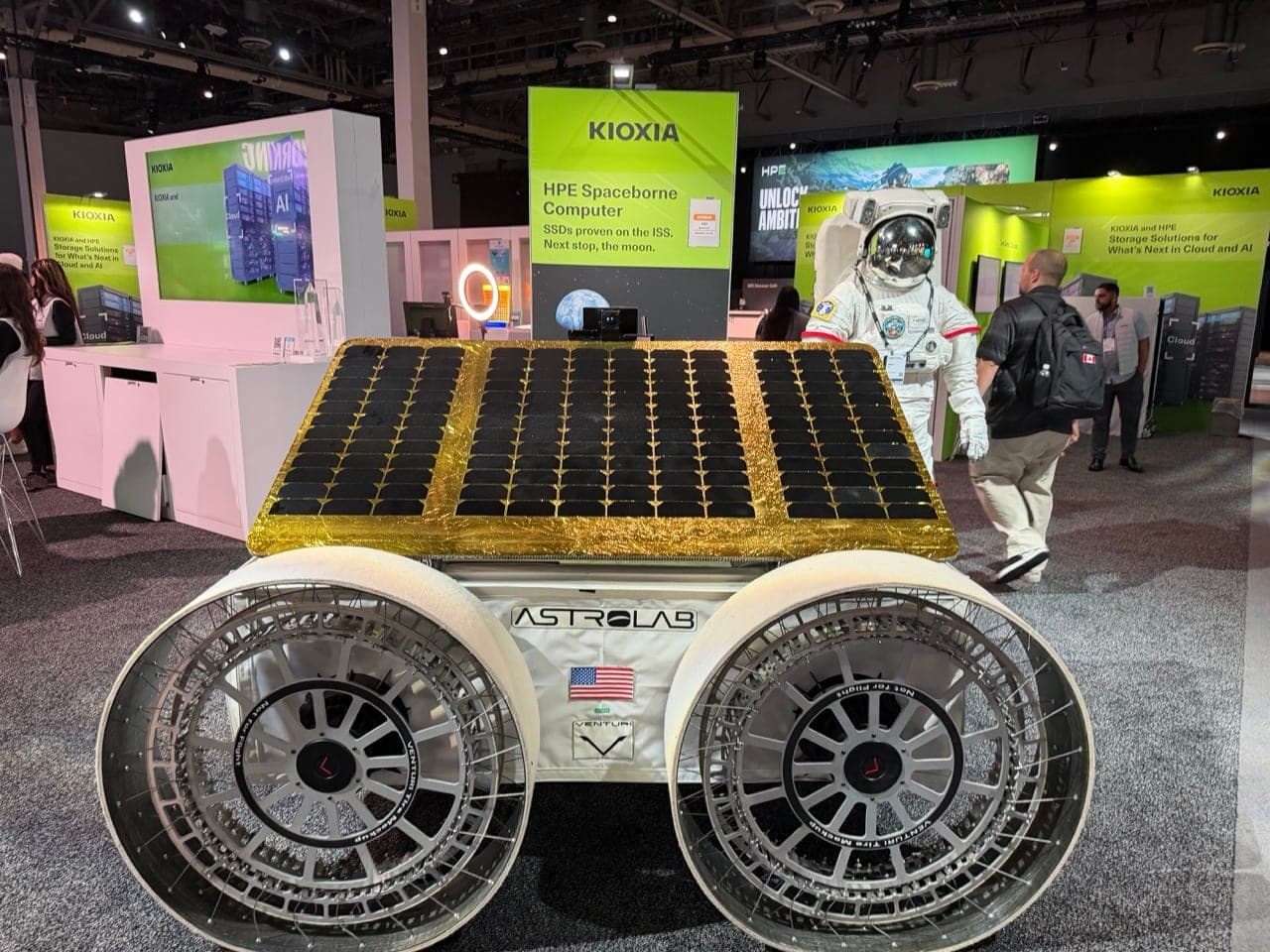 A full-size mockup of Astrolab's FLIP rover with gold-trimmed solar panel and large wire wheels on display at HPE Discover, with an astronaut suit and a Kioxia sign behind it