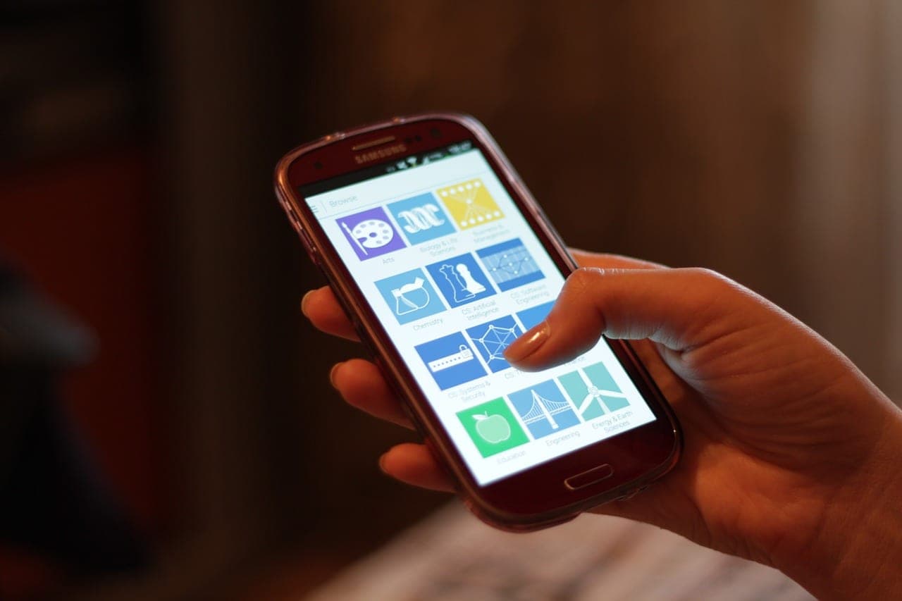 A person's hand holding a smartphone and scrolling through a grid of colorful app icons