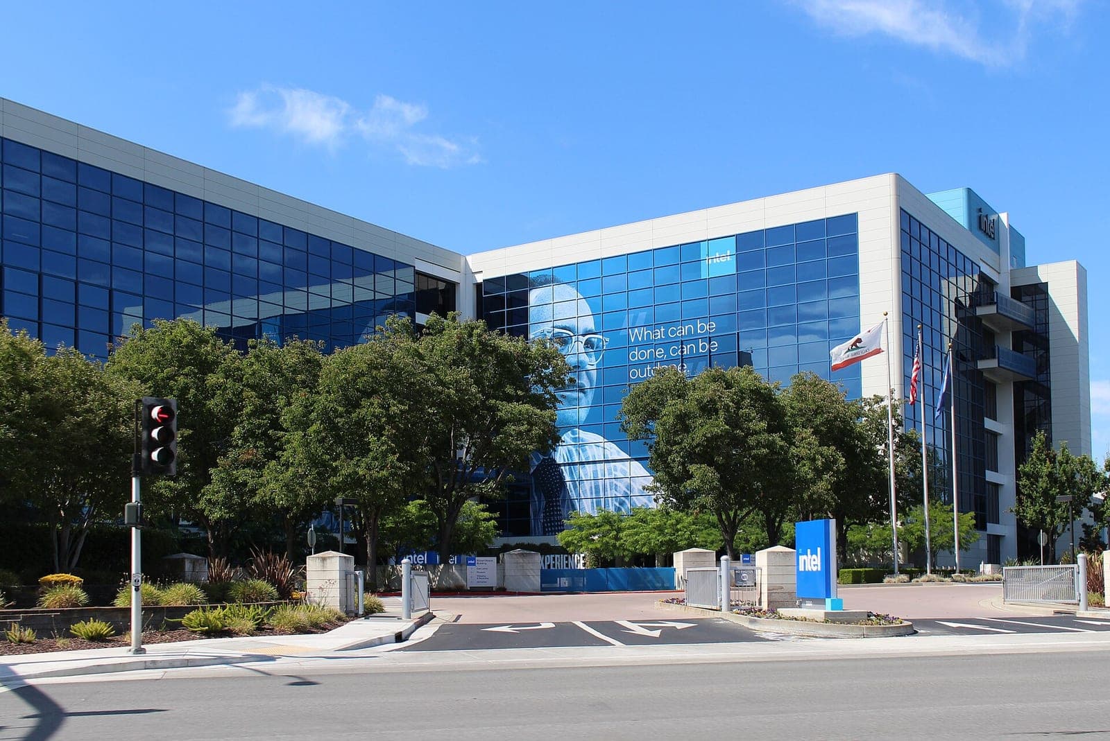 The glass front of an Intel office building in Santa Clara, California, with the blue Intel sign at the entrance and a large banner on the facade