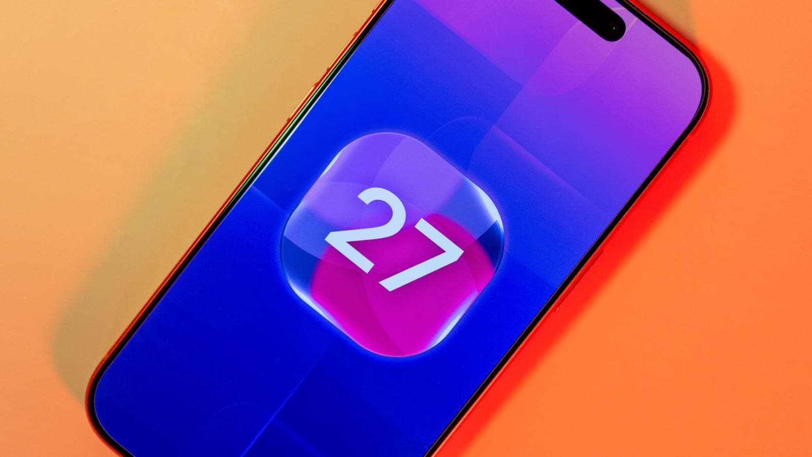 A red iPhone displaying the number 27 in a glowing app-icon style graphic on its screen, photographed at an angle against an orange background.