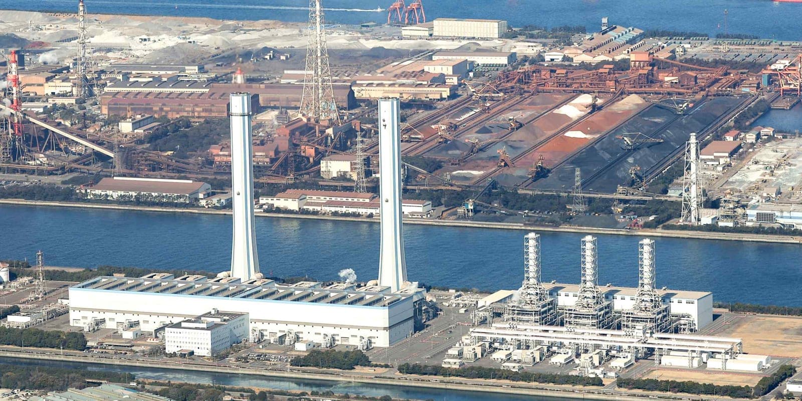 Aerial view of a large coastal power plant complex in Japan with tall chimney stacks, industrial buildings, and a waterway
