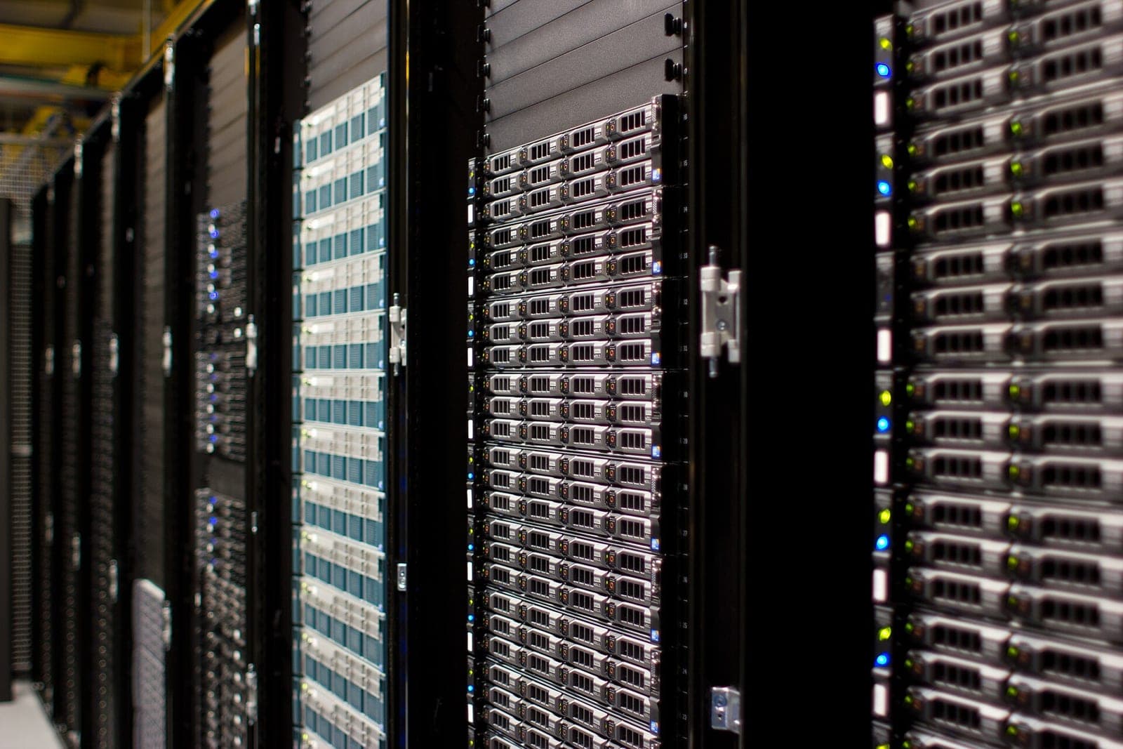 Rows of black server racks filled with stacked servers and glowing blue and green status lights in a data center aisle