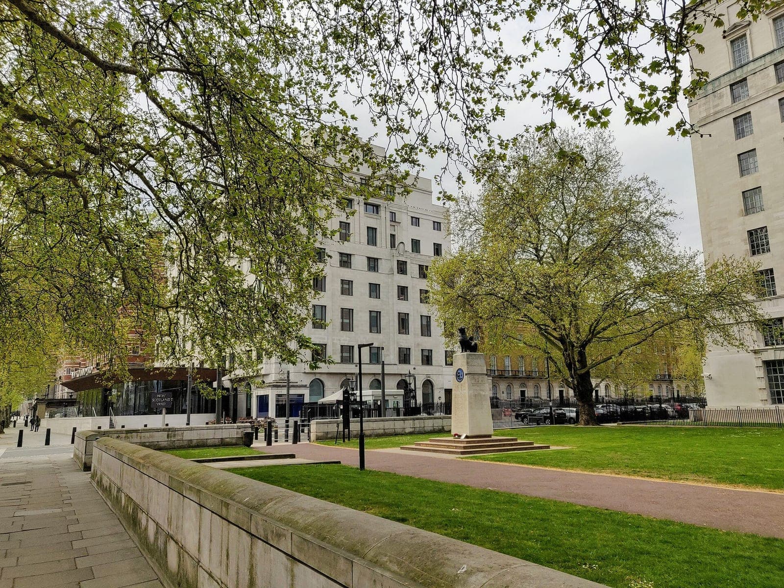The white stone New Scotland Yard building on London's Victoria Embankment, seen through spring trees across a public garden