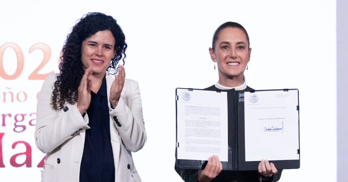 President Claudia Sheinbaum holds up the signed decree in an open folder while legal adviser Luisa María Alcalde applauds beside her on stage