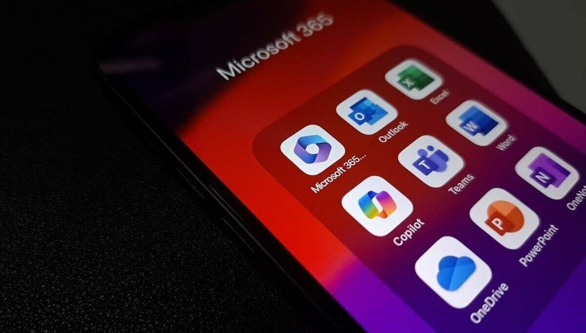 A smartphone screen showing a Microsoft 365 app folder with Outlook, Word, Excel, Teams, Copilot, PowerPoint, OneNote and OneDrive icons