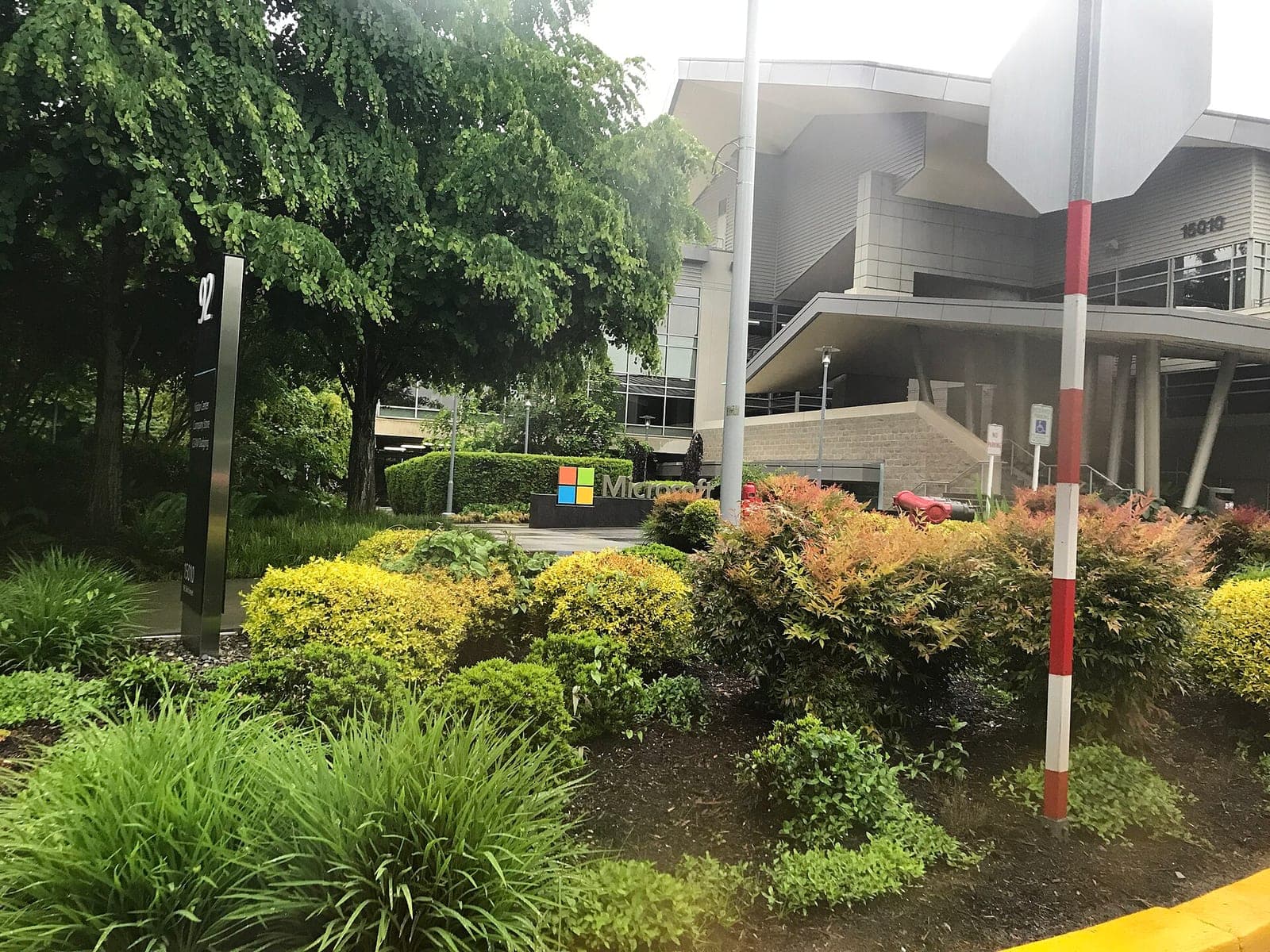 The Microsoft logo sign in front of the Visitor Center, Building 92, on the Microsoft campus in Redmond, surrounded by trees and shrubs