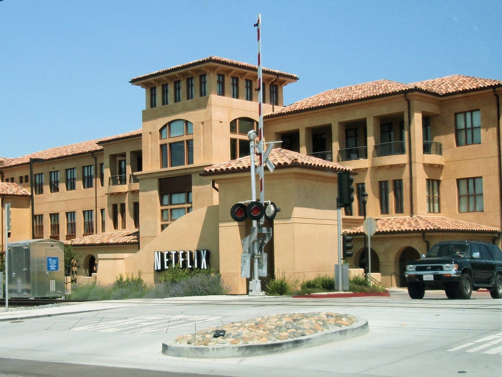 A Netflix headquarters building in Los Gatos, California, photographed in 2008, with a Netflix sign at the entrance next to a railroad crossing