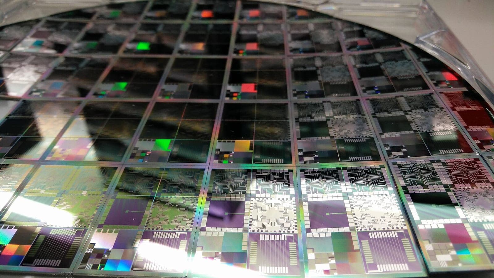 A close-up of a semiconductor wafer showing multiple colorful chip dies reflecting light